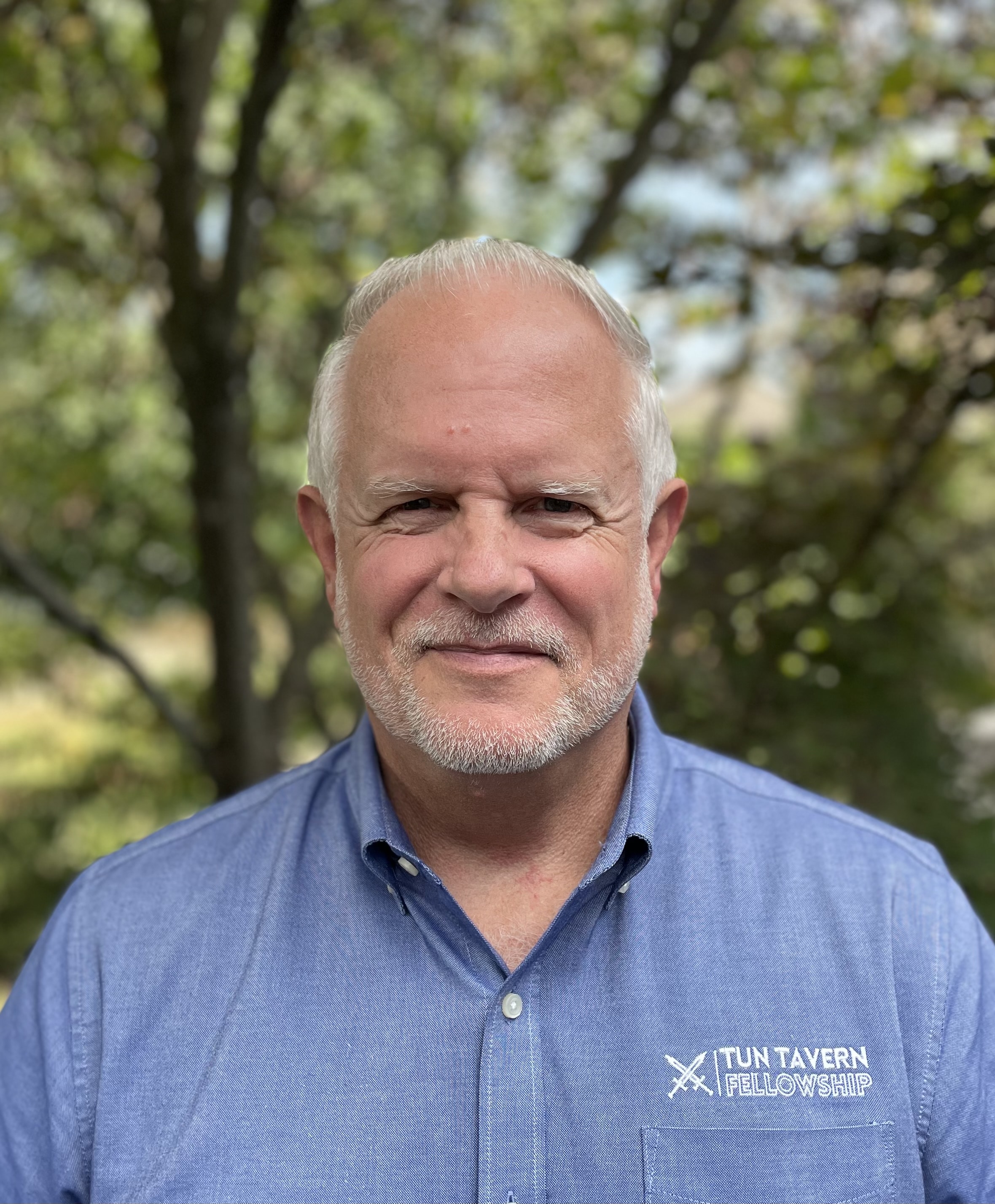 Director of Tun Tavern Fellowship faces camera for headshot with trees in the background.